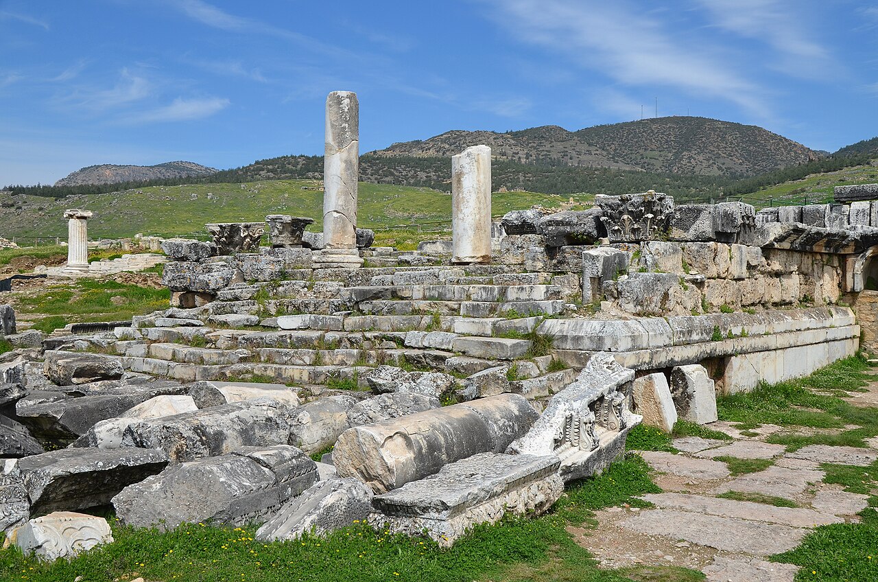 Restos del templo de Apolo en Hierápolis, con escalones, dos fragmentos de columnas y bloques tallados ante las colinas
